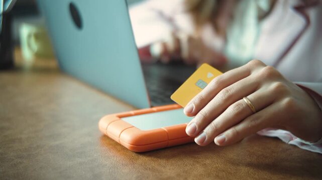Close-up of an anonymous woman's hand holding a credit card while making an online purchase, highlighting digital payment, e-commerce, and secure financial transactions using modern technology.
