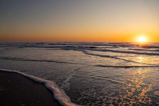 Golden sunrise reflecting on ocean waves with seafoam on wet sand, Corolla, North Carolina, Outer Banks (OBX)