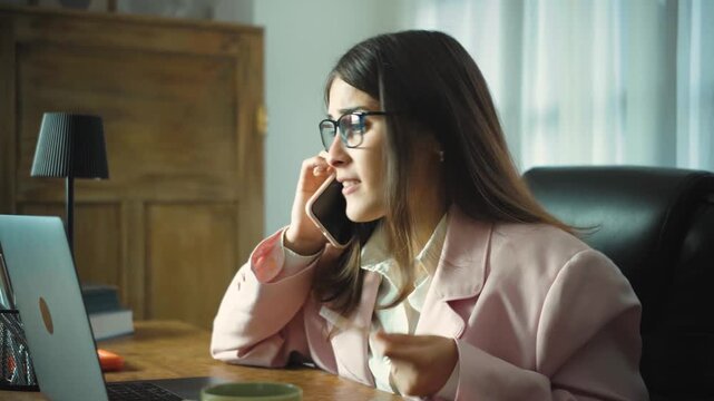 Young Hispanic woman in her office talking on the phone with a credit card company, expressing frustration while making a complaint and trying to resolve a billing or payment issue during her workday.
