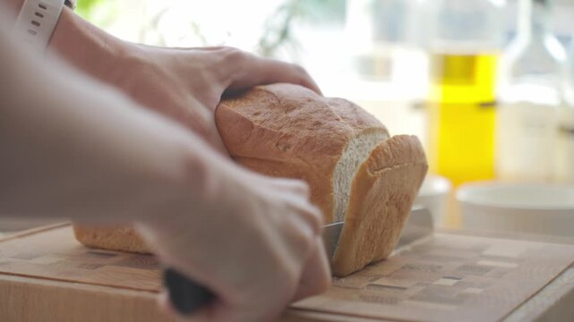 Hands slice loaf of bread on cutting board in kitchen. Concept of bread preparation and home cooking