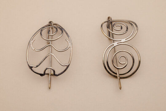 Two elegant silver hair barrettes with unique designs, one resembling a leaf and the other featuring a double spiral motif, display on a neutral background