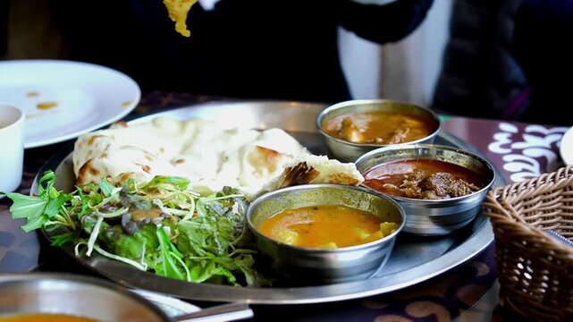 Close up of hands scooping potato from vegetable curry with a spoon and dipping naan bread