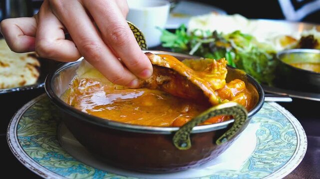 Close up of hands dipping freshly baked naan bread into creamy shrimp curry