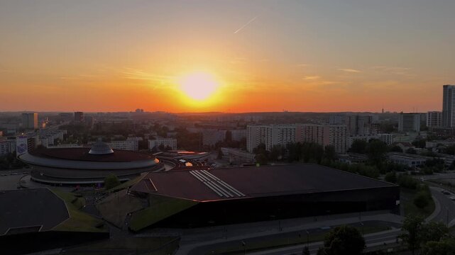 Aerial drone view of Spodek Arena and the Katowice city center during a colorful sunset. Modern architecture, urban skyline and golden hour over Silesia, Poland.