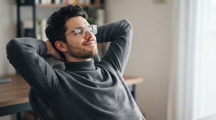 Obraz premium Satisfied young male freelancer wearing glasses relaxing in comfortable chair with hands behind head and closed eyes enjoying peaceful break at home office after finishing successful project.