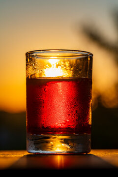Refreshing red cocktail in glass at sunset, closeup. Chilled red alcoholic drink with drops in glass against warm golden sunset background. High quality commercial food and beverage photography