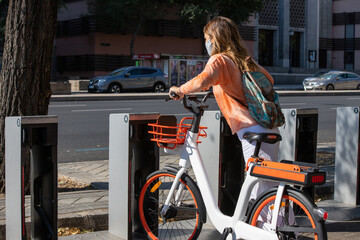 Naklejka premium Unrecognizable female taking modern rental bike from parking lot on sunny day in Madrid, Spain