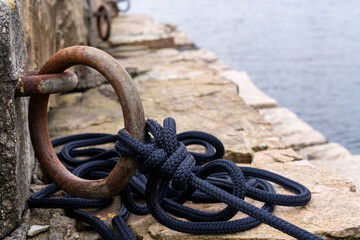 Obraz premium Rusty mooring ring with black rope on stone pier