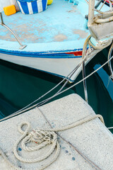 Fototapeta premium Close up of a thick mooring rope tied around a dock cleat with a white boat hull in the background.