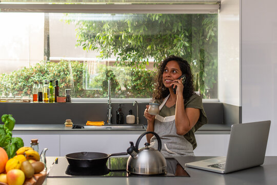 Hispanic woman talking on smartphone while working in modern kitchen