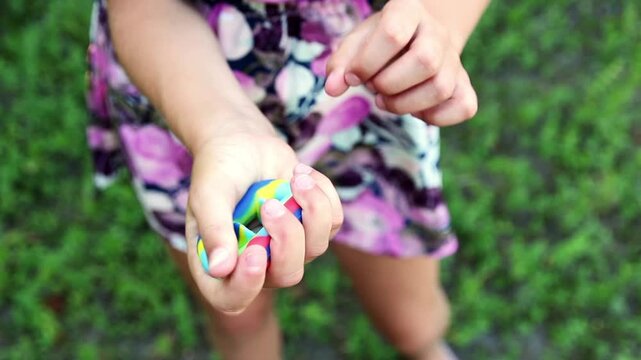 Close up of child hands holding and squeezing colorful rainbow popit snapper toy outdoors. Girl playing with trendy anti stress fidget toy