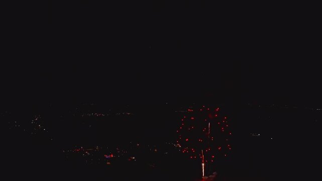 People gather on the streets to watch a fireworks display in the city at night. Bright colors fill the sky as fireworks explode, creating a festive atmosphere.