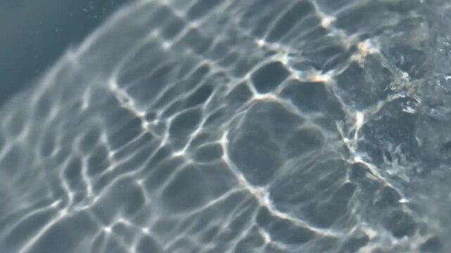 Water Reflection Patterns: Abstract view of sunlight refracting through clean, clear water, creating mesmerizing wave-like patterns and light play on the surface.