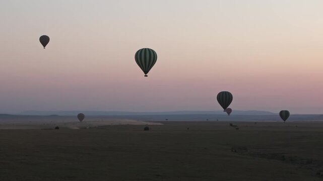Slow motion aerial landscape of Maasai Masai Mara national park wildlife reserve in Kenya, Africa as hot air balloon safari above golden sunlight sunrise morning rise above safari African grassland 4k