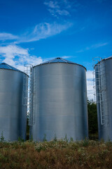 Three modern corrugated steel grain silos standing on an agricultural field. shot of shiny silver storage tanks with safety ladders under a beautiful blue sky with white clouds. © Fotoforce