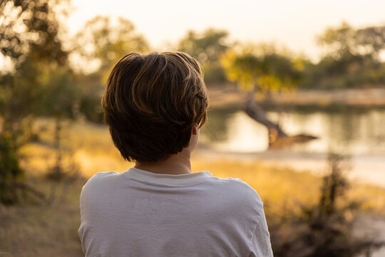 rear view of young boy looking at Zambezi River at sunset, Zambezi National Park, Zimbabwe, Africa