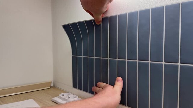Hands applying flexible dark blue tile sheet on kitchen wall, close up home renovation detail, diy interior upgrade, clean modern backsplash installation