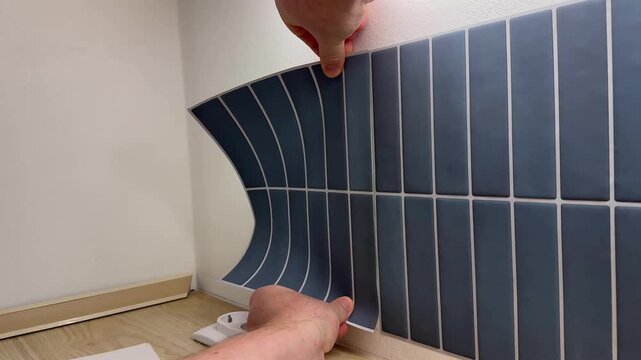 Hands apply flexible blue tile sticker to a wall, showing careful alignment and smoothing, clean home improvement scene with practical diy mood