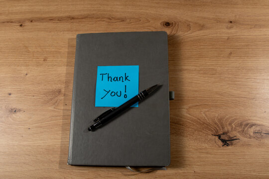 a closed notebook with a blue sticky note with the message tank you a dark pen on it, waiting to be opened and filled with writing, creativity, concept or design ideas. Concept of gratitude.
