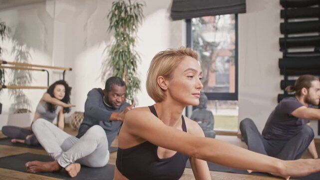 Group of yogi people sitting in padmasana pose. Multicultural people sitting at mats and doing yoga pose with hands. Multiethnic people practicising at yoga studio. People at yoga session.