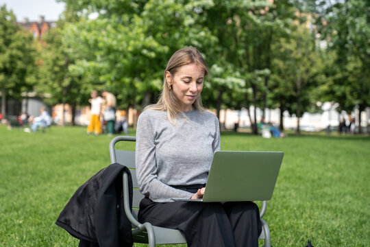 Relaxed focused middle aged business woman in city park using laptop. Distance working, digital nomad mobility, outdoor office in nature