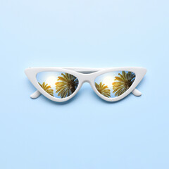 Obraz premium Stylish sunglasses on light blue background. Sky and tropical palm trees reflecting in lenses