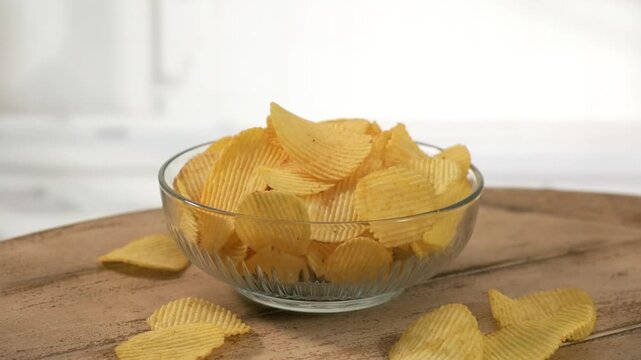 Ridged potato chips in glass bowl on light table, minimal composition, copy space