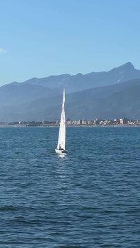 Sailboat sailing at Tuscany coast panoramic view coastline with beaches and mountains at sunny day, Viareggio, Versilia, Italy.	