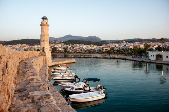 The historic Egyptian lighthouse stands at the end of the stone breakwater of the Venetian harbour of Rethymno, with fishing boats on the island of Crete in Greece.