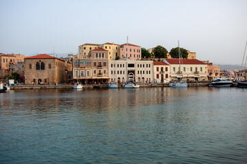 Obraz premium Colourful Venetian houses line the waterfront of the old harbour of Chania with boats and reflections on the island of Crete in Greece, a popular travel destination.