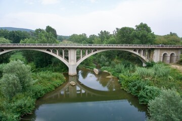 Fototapeta premium Concrete arch bridge reflected in the Fluvia river