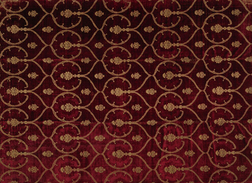 Antique deep red velvet fabric background with ornate golden floral damask pattern. Luxurious vintage textile texture.