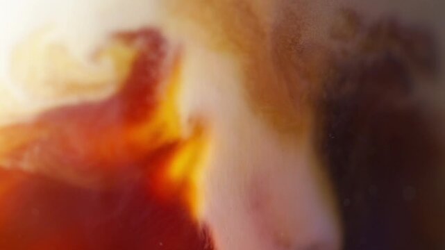 Coffee and milk swirling together creating creamy cappuccino texture with rich foam in macro close up slow motion