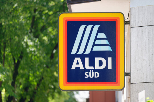 Cologne, Germany July 15 2026: Close-up of the official blue and orange Aldi S&uuml;d corporate logo sign mounted on a building storefront with a blurry green tree background.
