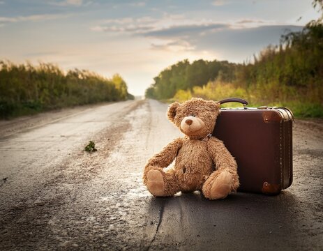 ragged teddy bear by a suitcase at the side of a dirty road