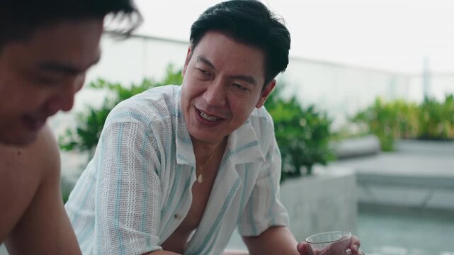 Happy gay couple talking and laughing by a modern rooftop pool
