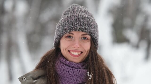 A beautiful young woman in winter clothes is happily spending her free time in a snowy forest. She enjoys the first snow. Active winter recreation.