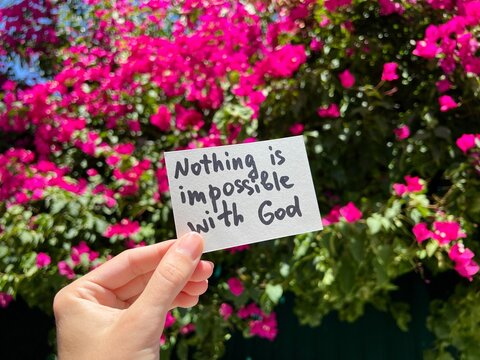 Nothing is impossible with God - christian card in the hand and pink flowers on background, religion concept