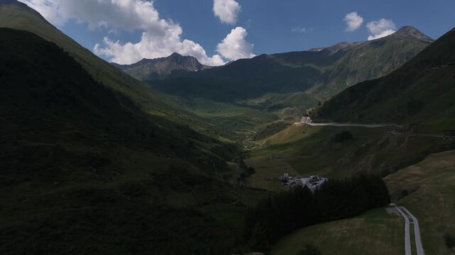 serene mountains in a valley with road and clouds, aerial view of green grass and blue sky, nature and travel scene, peaceful landscape with rocks and concrete, Andermatt