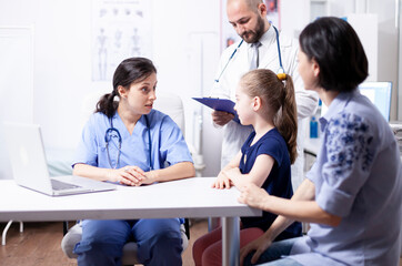 Fototapeta premium Nurse listens to a child during a hospital consultation while a doctor takes notes, supporting pediatric examination and treatment planning, keeping the focus on consultation, healthcare and the.