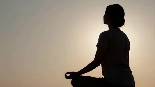 Silhouette profile of a person meditating in a zazen pose against a warm golden hour sunset light, 4K, Seamless loop, Copy space on the left