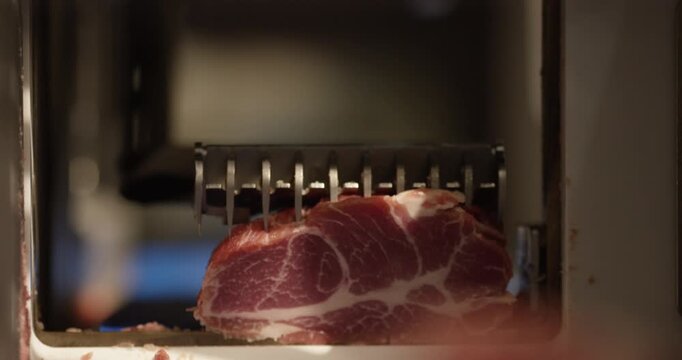 Freshly cut slice of marbled meat resting at the opening of a slicing machine in a butcher shop