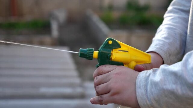 Child hands spraying water with a plastic spray bottle in the garden