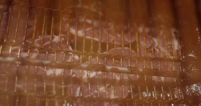 Marbled meat cutlets resting on metal racks inside a steamy smoking chamber at a meat processing facility