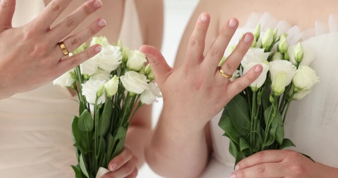 Lesbian marriage. Two brides with beautiful flowers showing their wedding rings indoors, closeup. Camera moving in