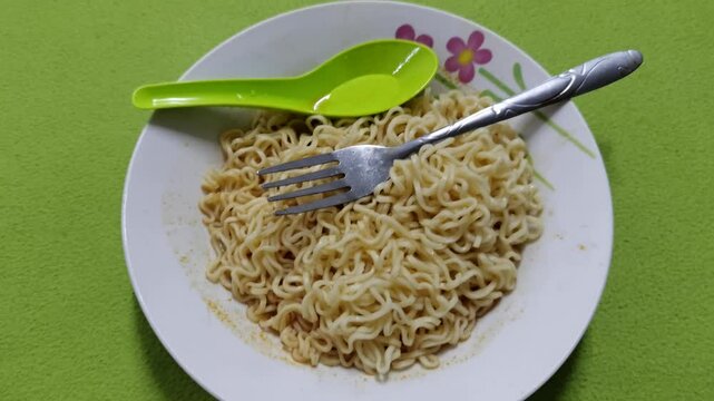 Instant fried maggie served on a ceramic plate with a fork and green spoon against a bright green background