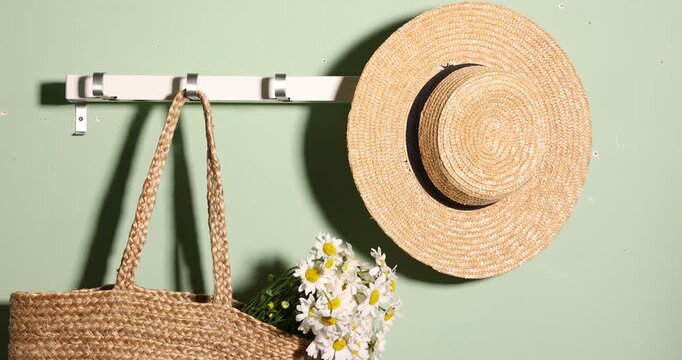 Woman hanging wicker bag with beautiful chamomile flowers onto hook near green wall, closeup
