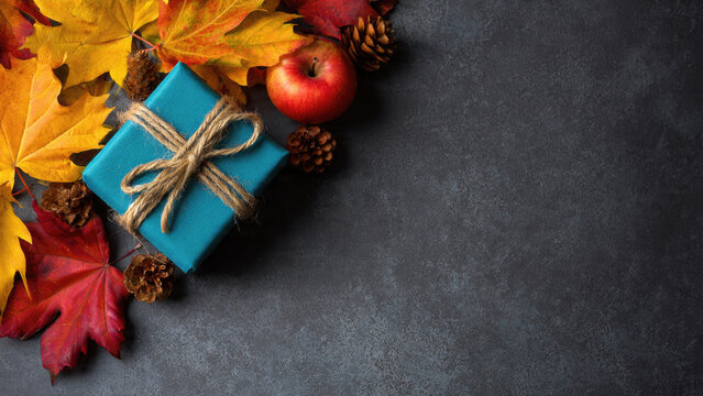 Autumn leaves gift box and apple on dark gray background fall seasonal composition