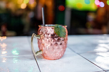 Copper mug filled with drink placed on white tile surface in social space © Marko