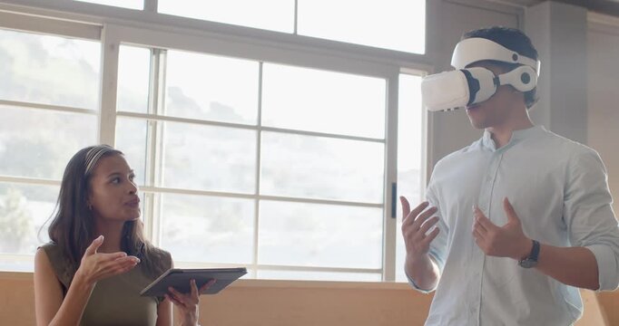 Diverse coworkers by grid windows woman with tablet raising hand, man mirroring motion in VR demo